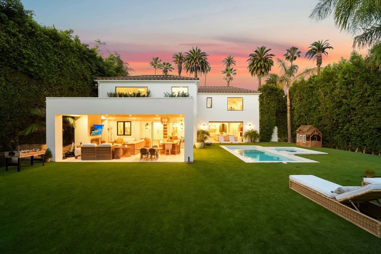 Twilight exterior with lit interiors opening onto a pool and palms